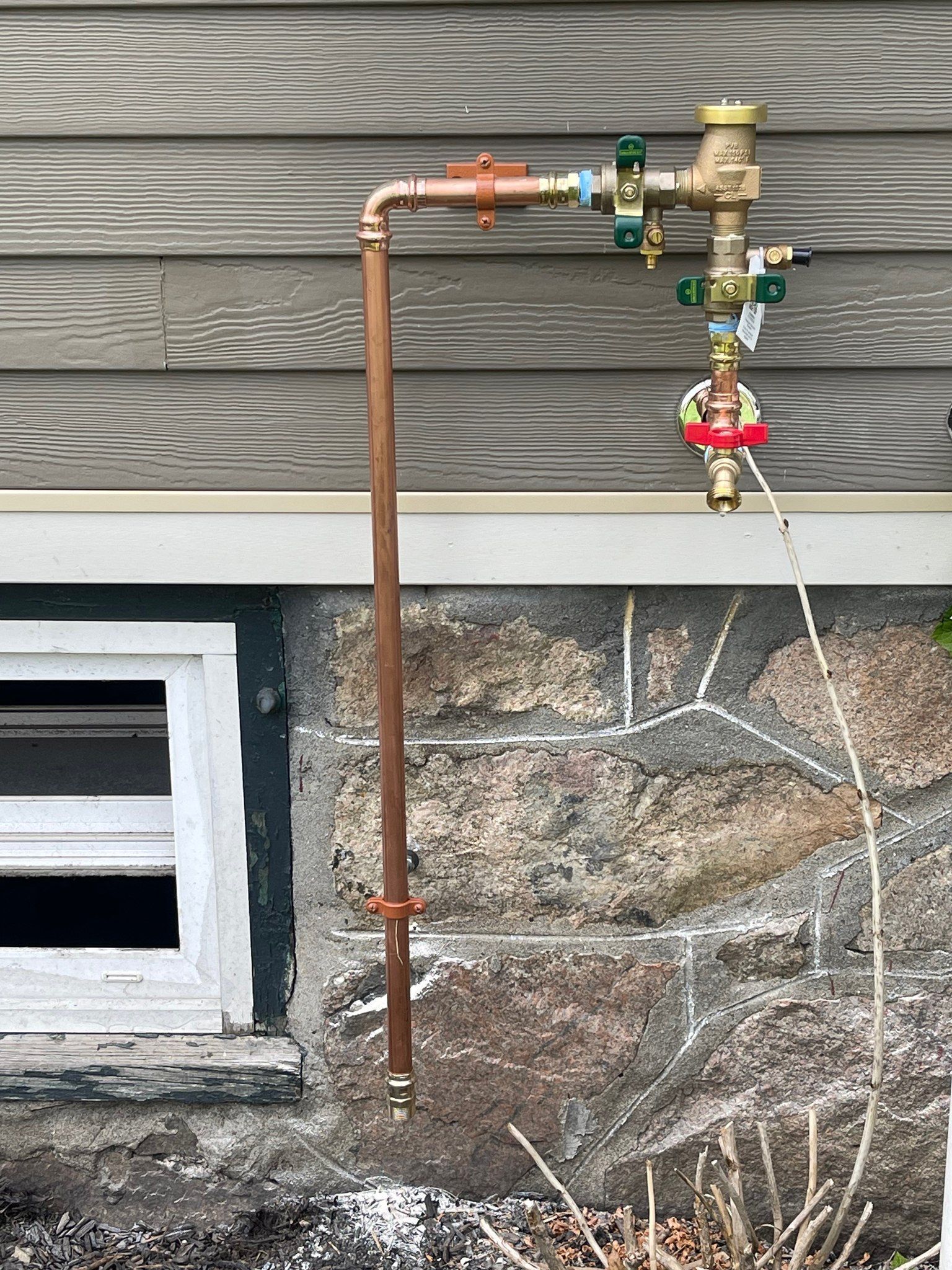 A copper pipe is attached to the side of a house next to a window.
