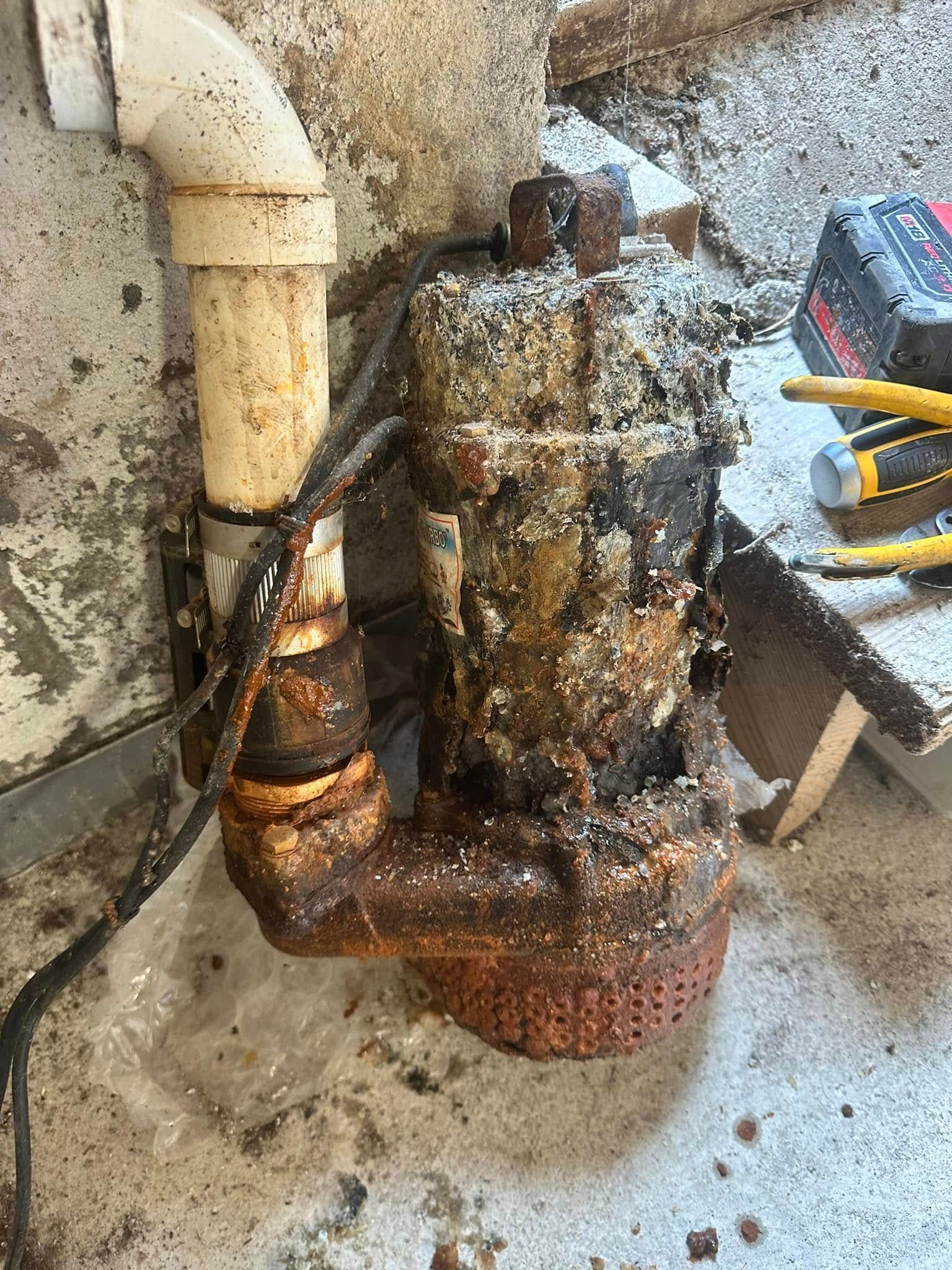 A rusty water pump is sitting on the floor next to a pipe.