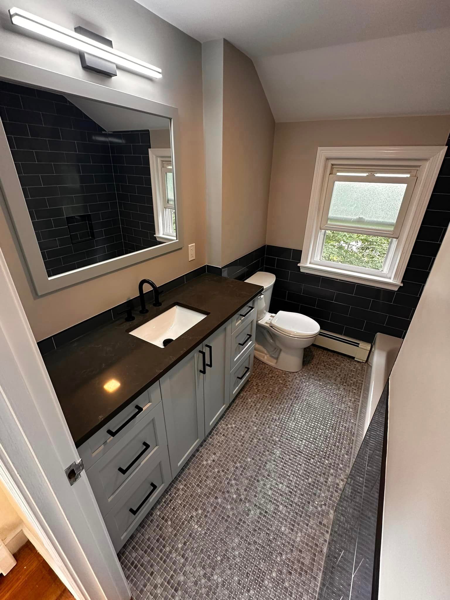 A bathroom with a sink, toilet, mirror and window.