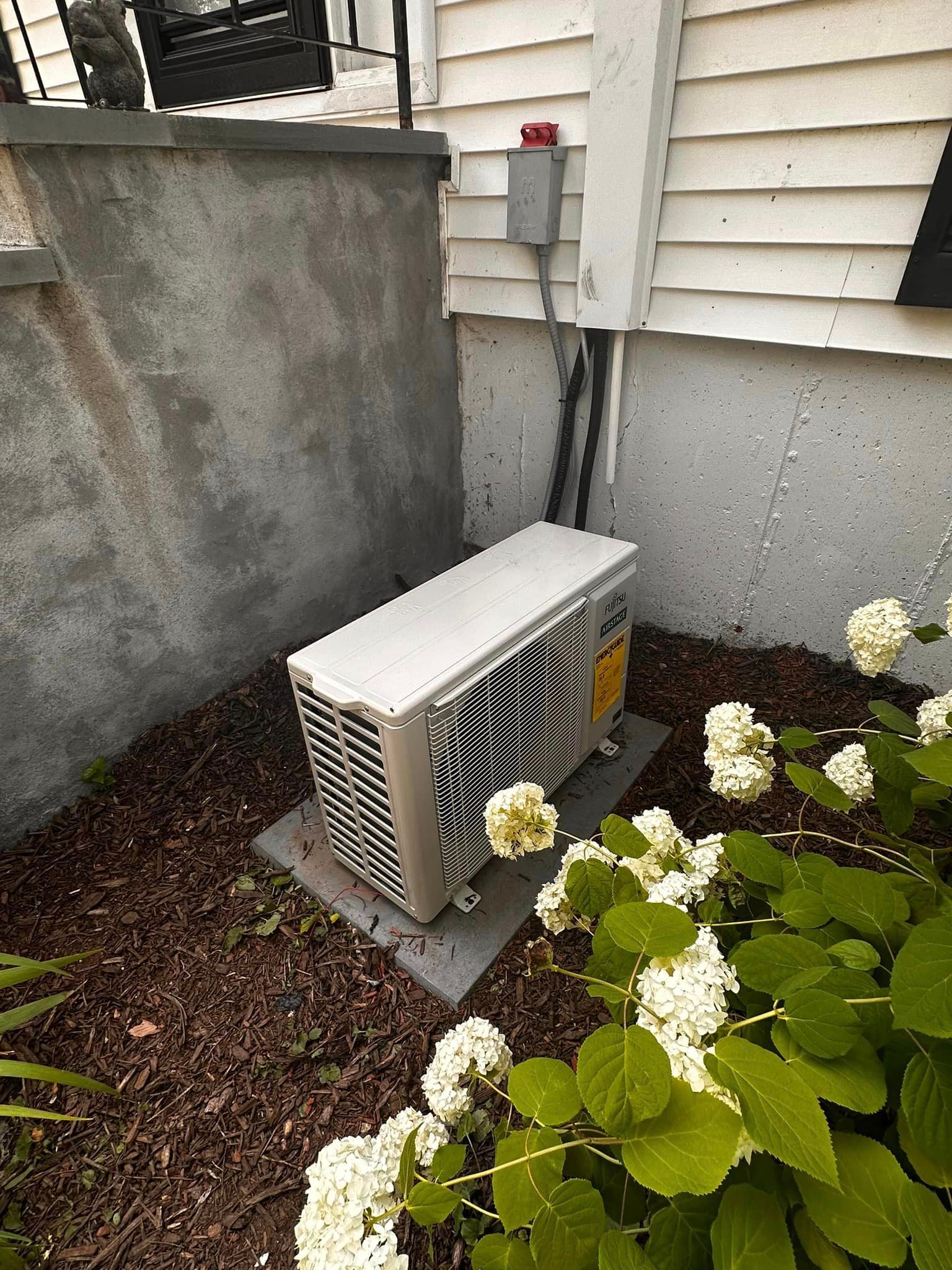 A white air conditioner is sitting in the dirt next to a white house.