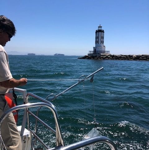 Person on a boat near a white lighthouse in blue ocean water
