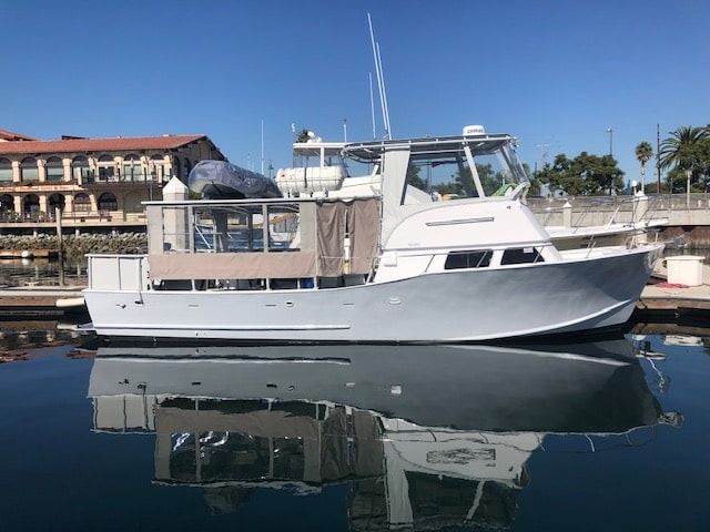 White motor yacht docked on calm water with its reflection visible.