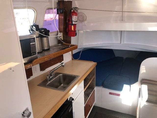 Compact cabin kitchenette with sink, microwave, coffee maker, and a small bed in the background
