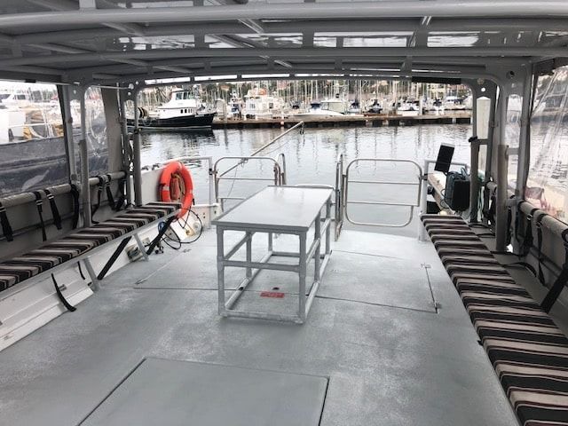 Empty boat deck with benches, a white table, and safety equipment on a gray floor.