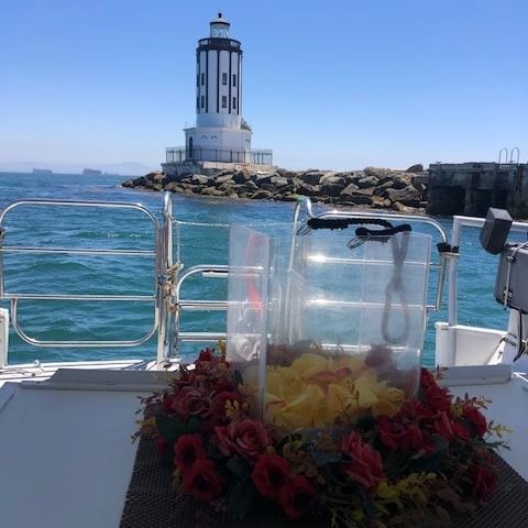 Boat view of a white lighthouse on a rocky breakwater, with flowers in a clear vase in the foreground