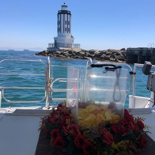 Boat deck with flowers and a clear bag, facing a striped lighthouse over blue water.