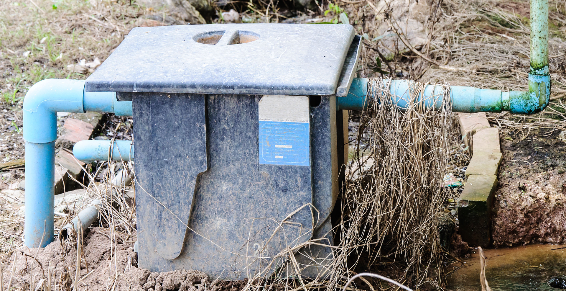 A concrete box with blue pipes attached to it is sitting in the dirt.