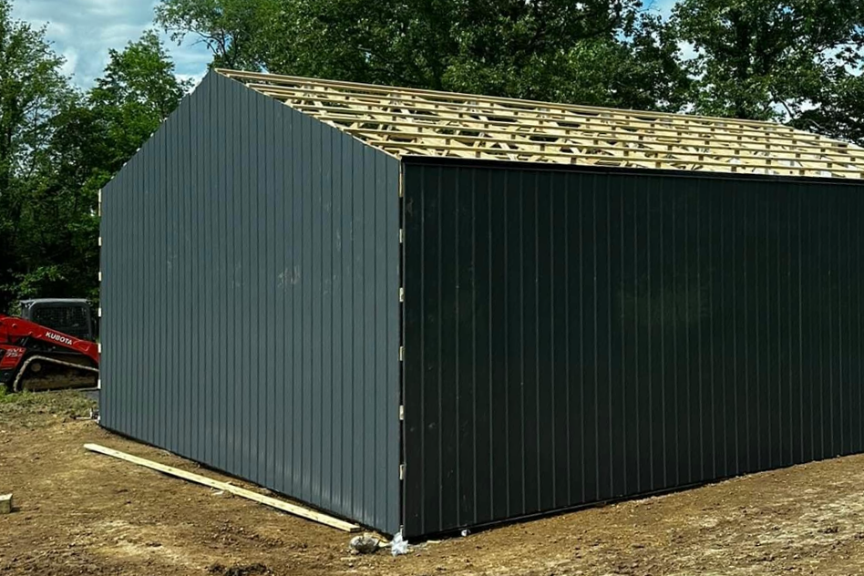 A pole barn with a wooden roof is being built in a dirt field.