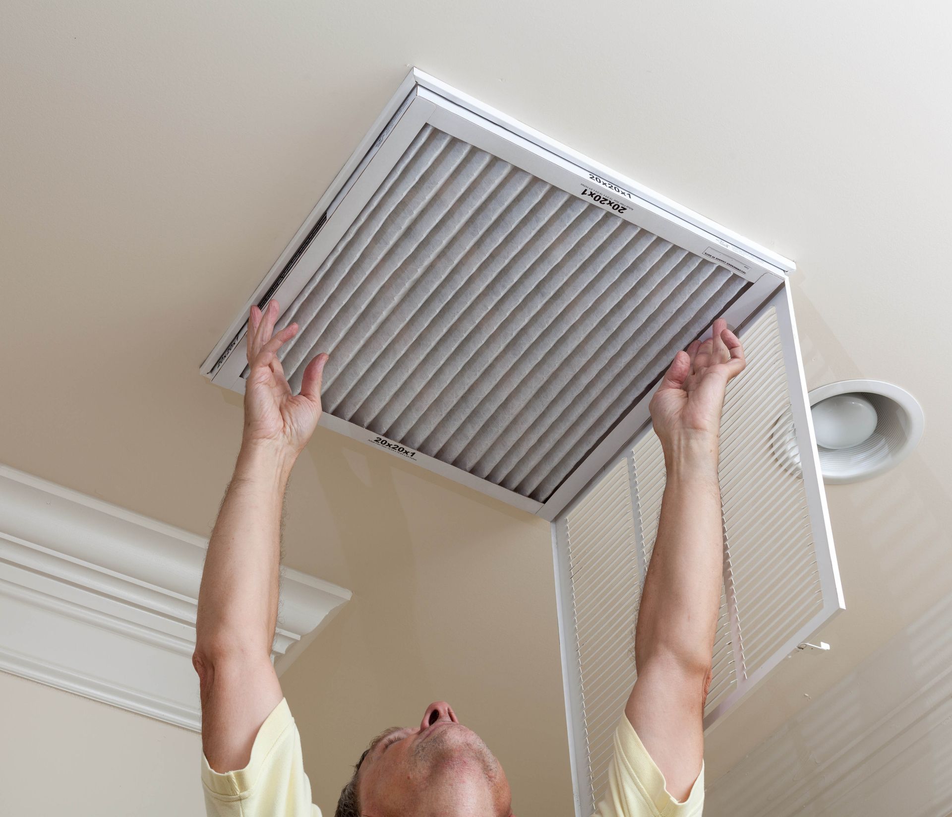 Person replacing a ceiling air filter with both hands raised.
