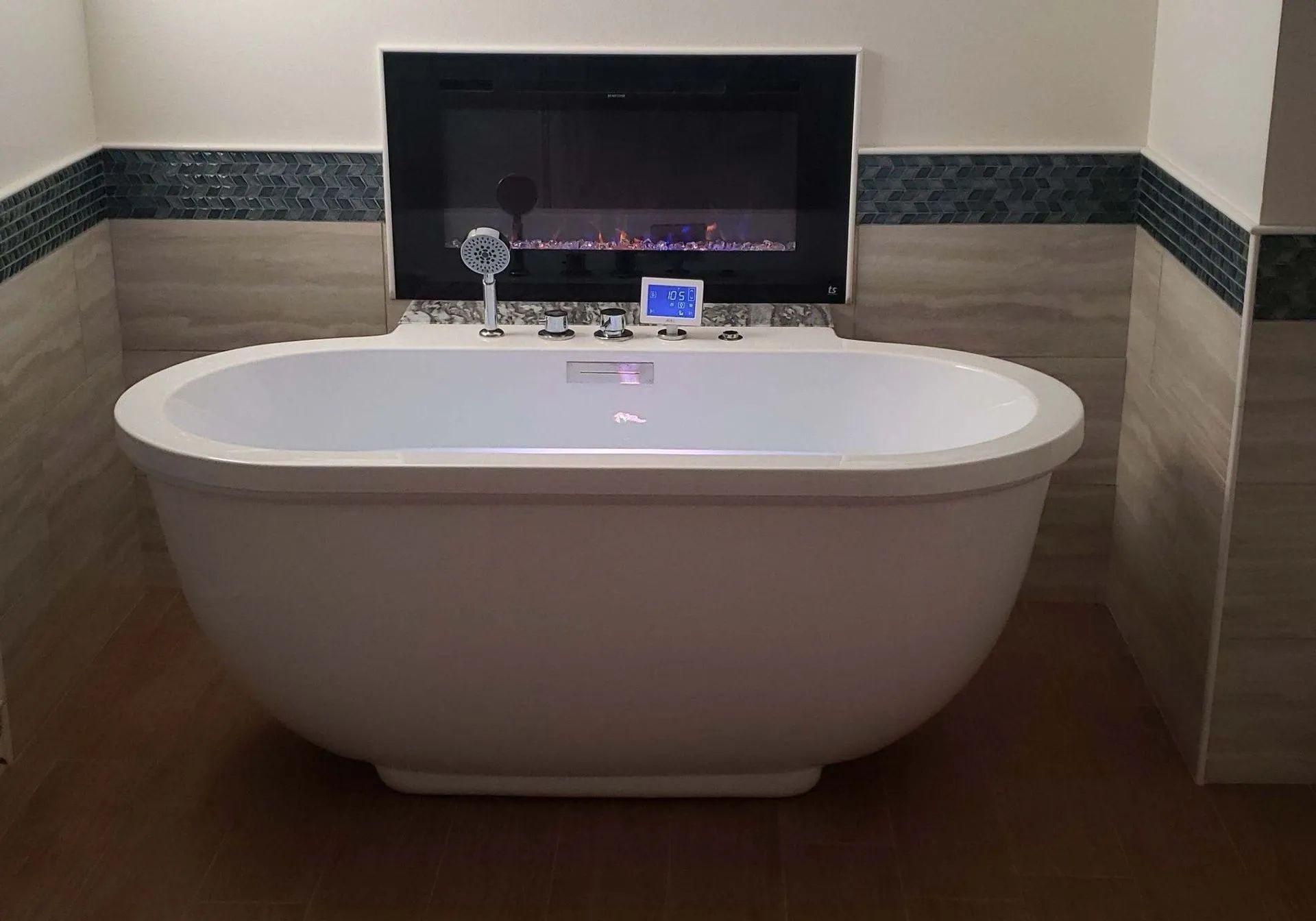 Freestanding white bathtub centered in a tiled bathroom beneath a dark-framed mirror and shelf