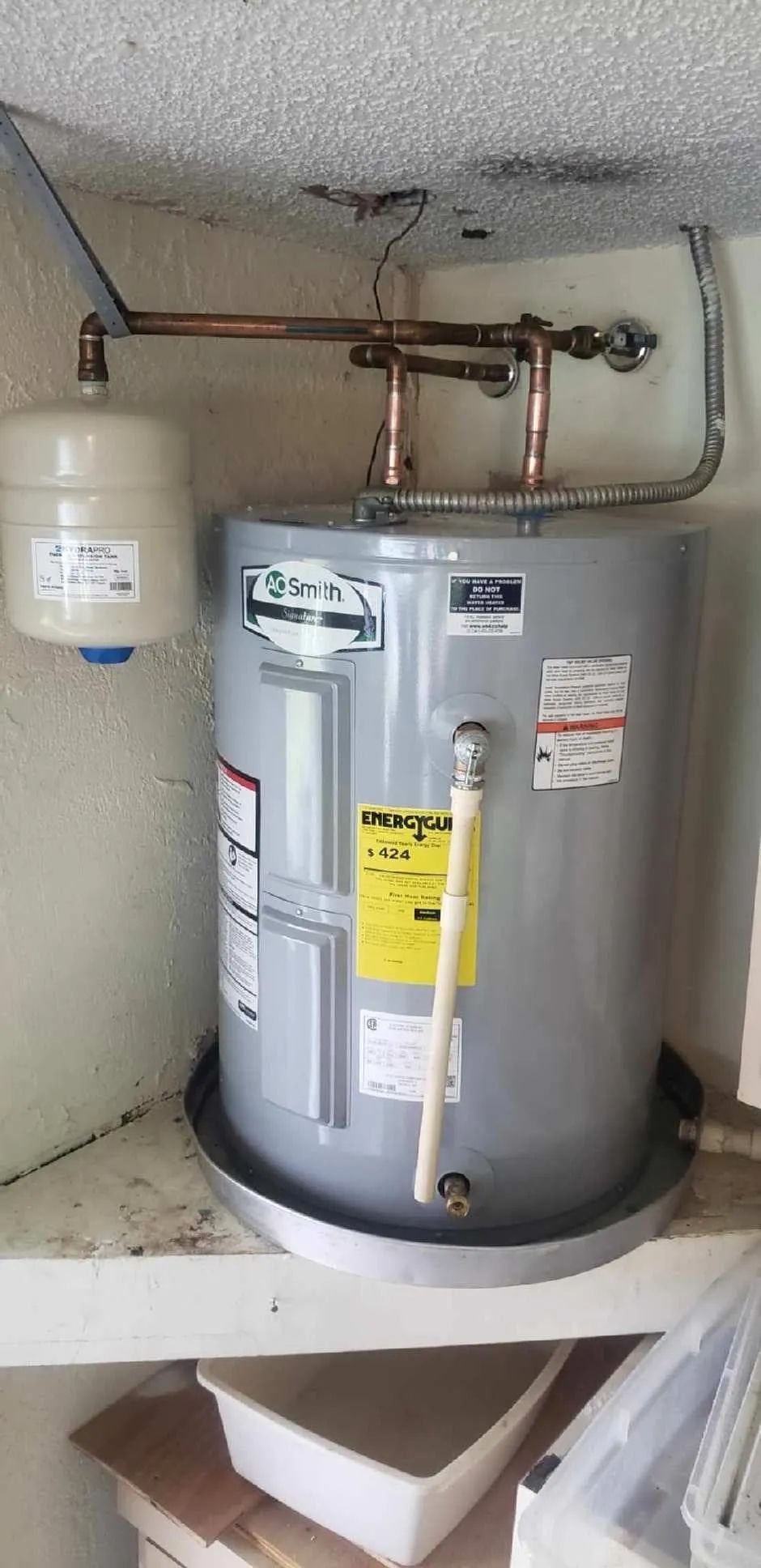 Water heater in a closet with exposed copper pipes and a tank, viewed from above.
