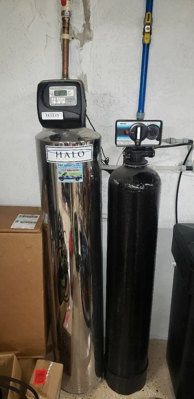 Two tall water treatment tanks with meters and pipes in a utility room