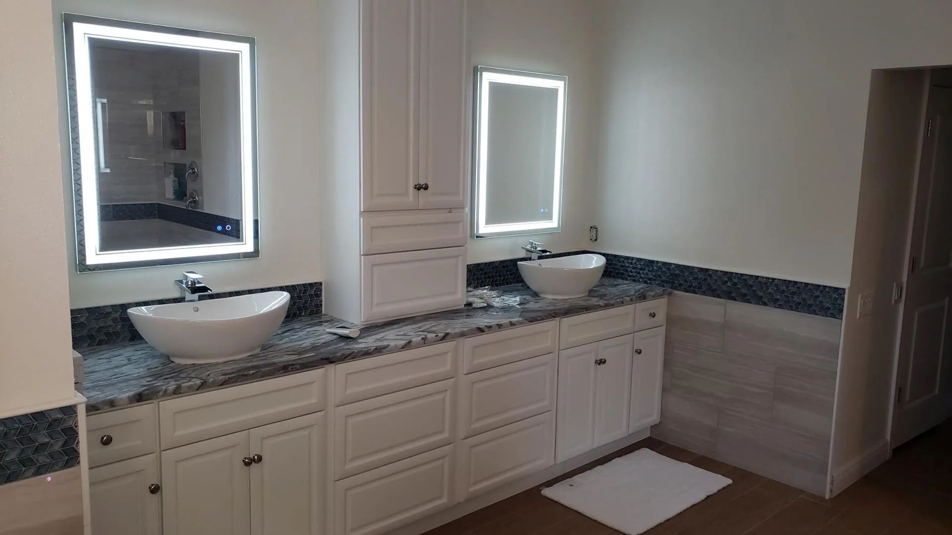 Modern double-vanity bathroom with illuminated mirrors, white cabinets, and granite countertop