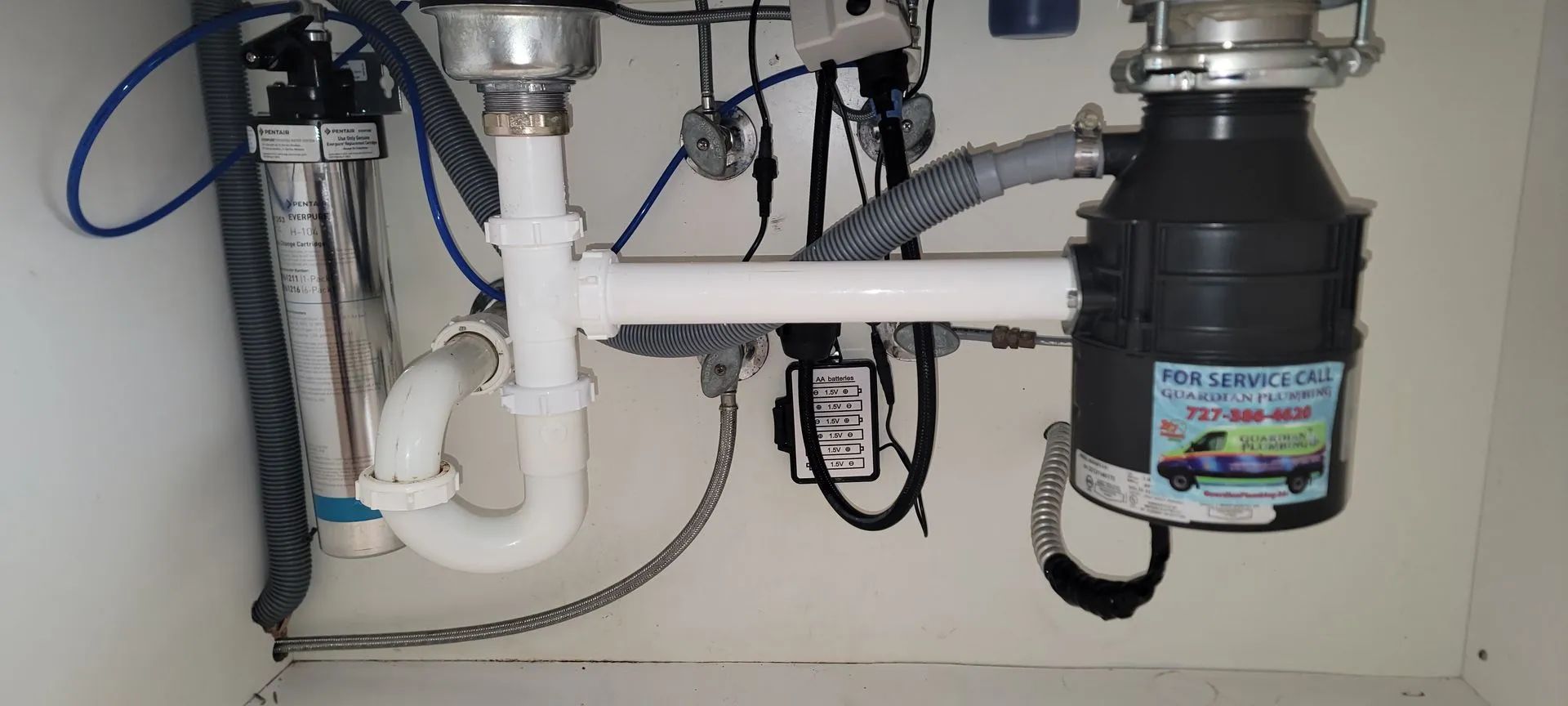 Under-sink plumbing with white PVC pipes, a black garbage disposal, and exposed drain lines.