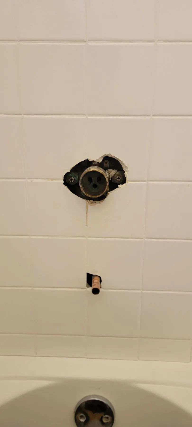 Partially tiled bathroom wall with exposed plumbing fixtures above a bathtub.