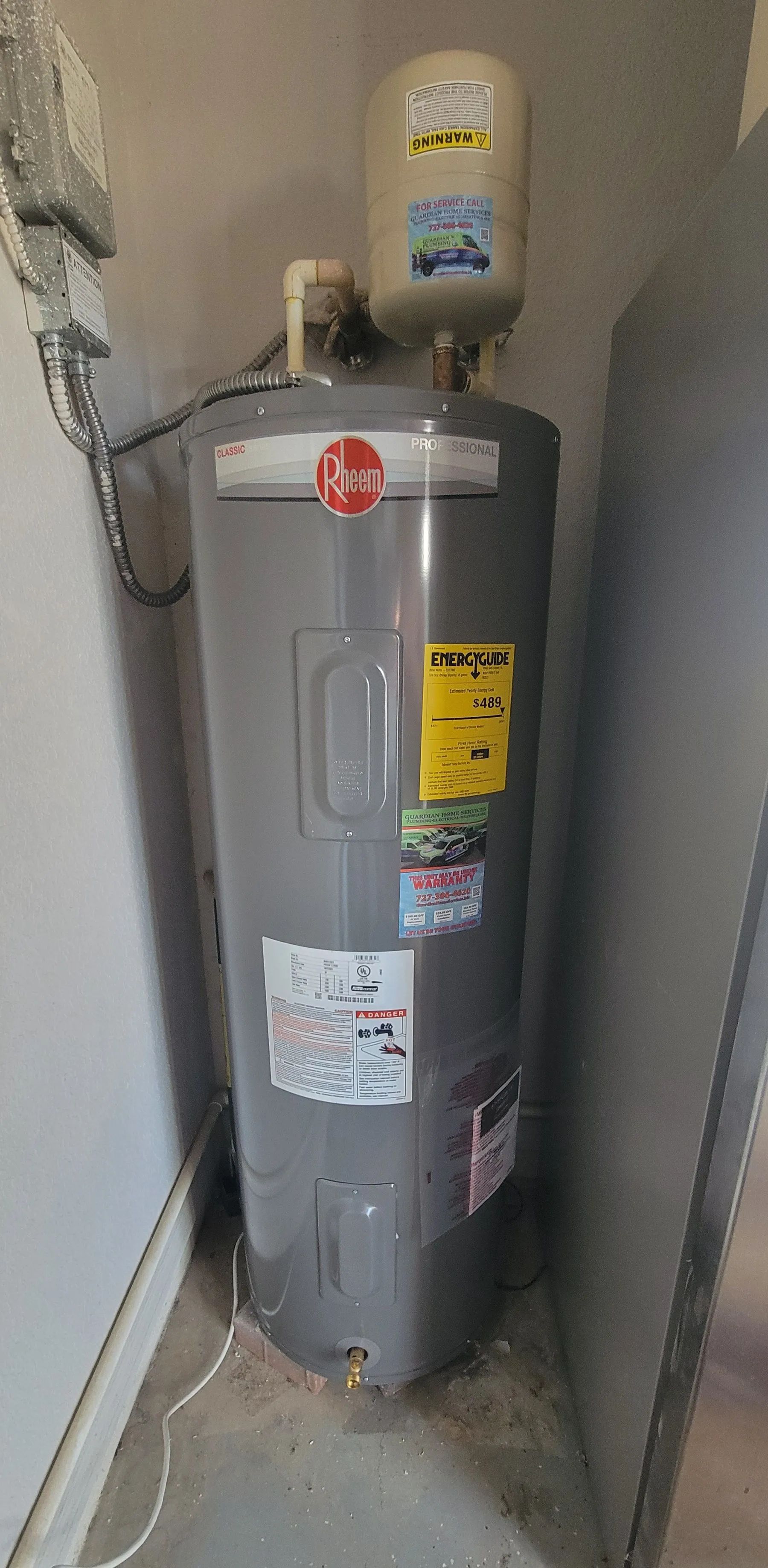 Gray water heater in a narrow utility closet with pipes and labels on top