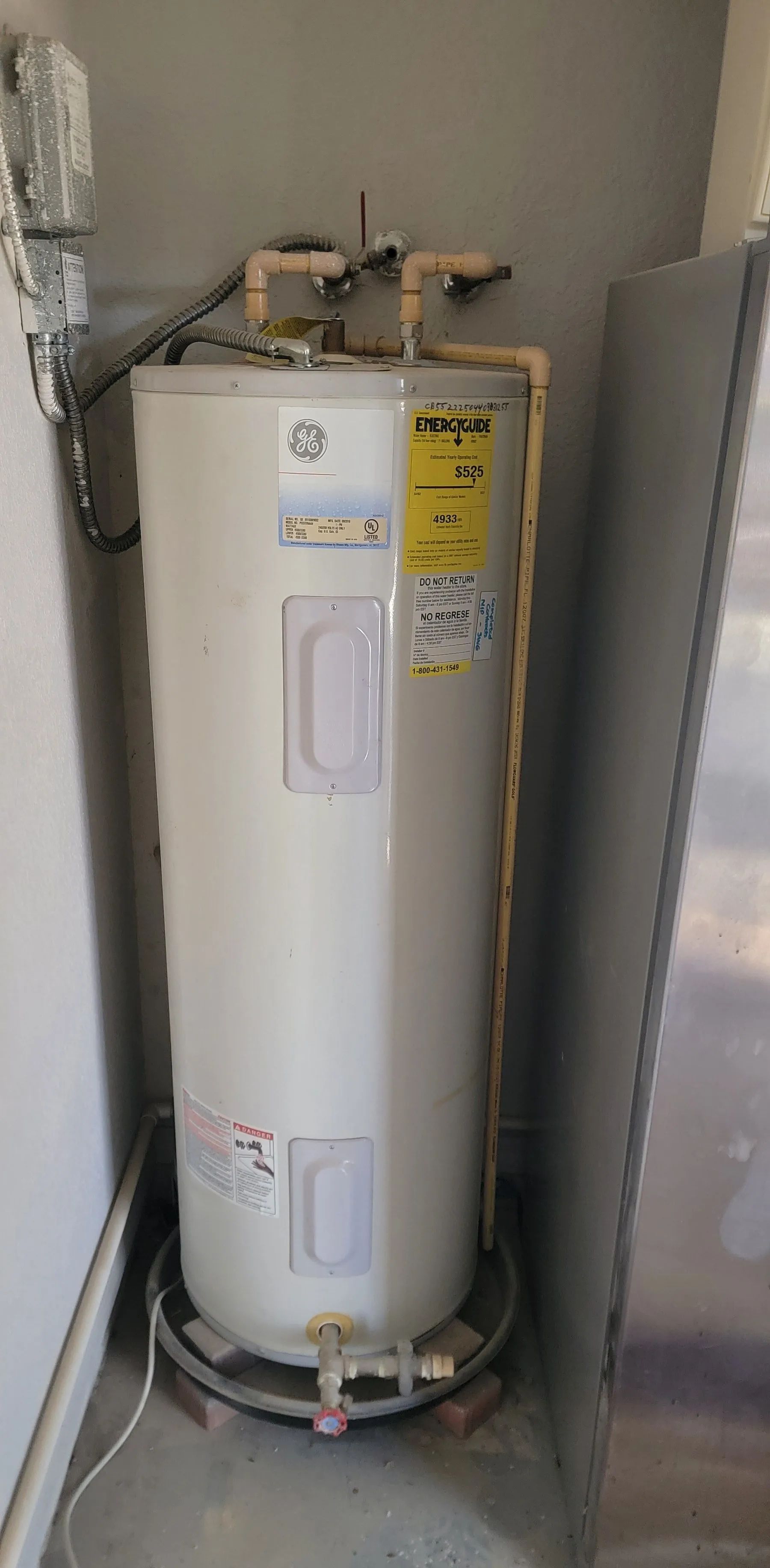 White water heater in a utility closet with pipes and warning labels