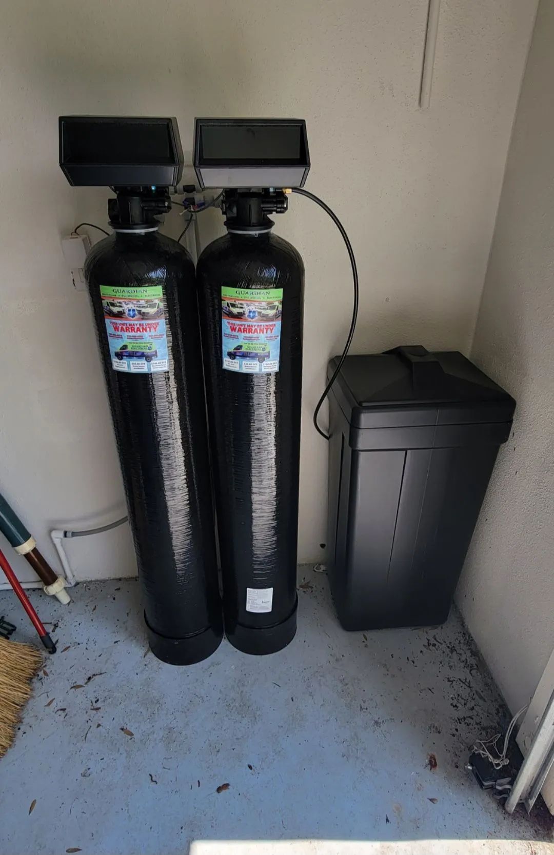 Two tall black water softener tanks beside a black utility cabinet in a small room