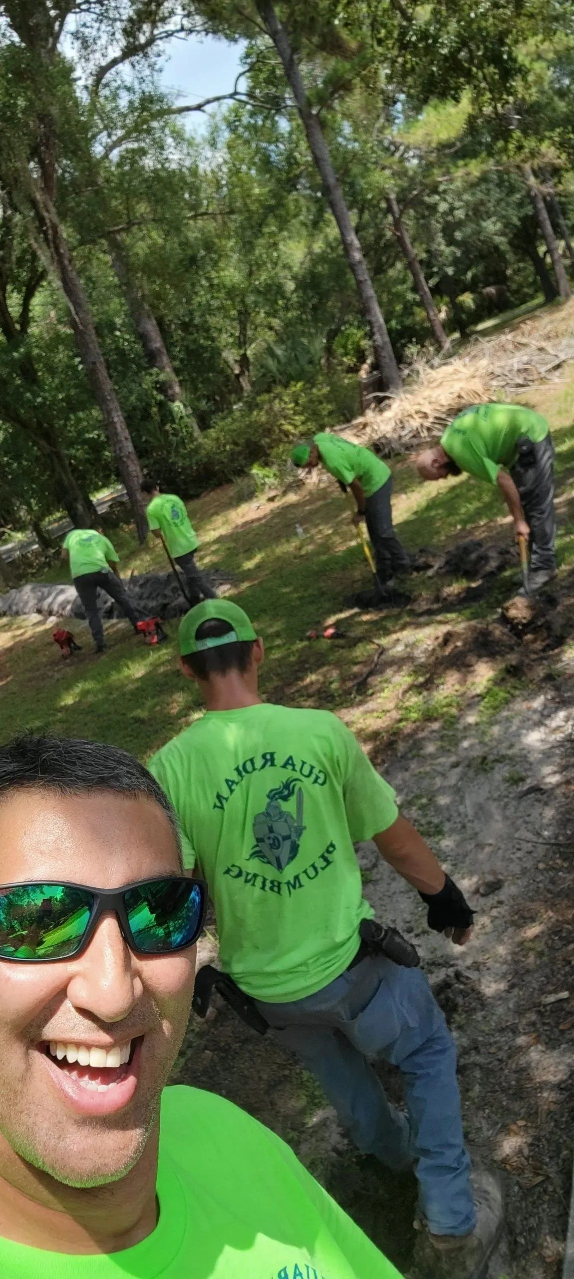 Group of people in bright green shirts hiking on a wooded trail, one smiling selfie in foreground