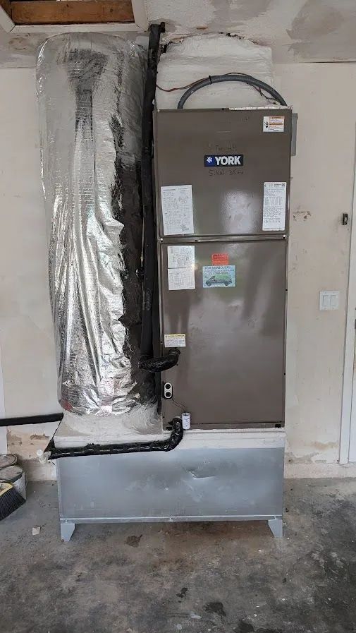 HVAC furnace with silver ductwork in a utility room, gray cabinet against a unfinished wall