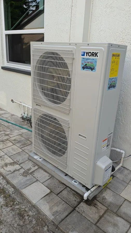 White YORK outdoor air conditioner unit beside a building wall on a paved patio