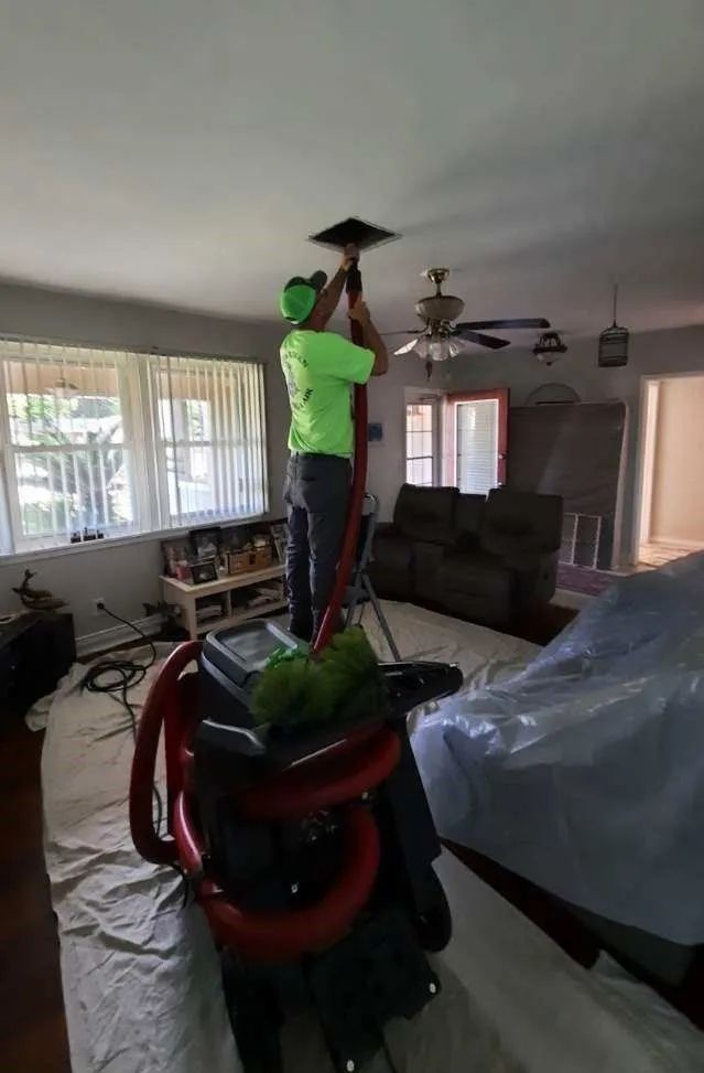 Person in a bright green shirt working on a ceiling fixture in a living room with furniture covered in plastic.