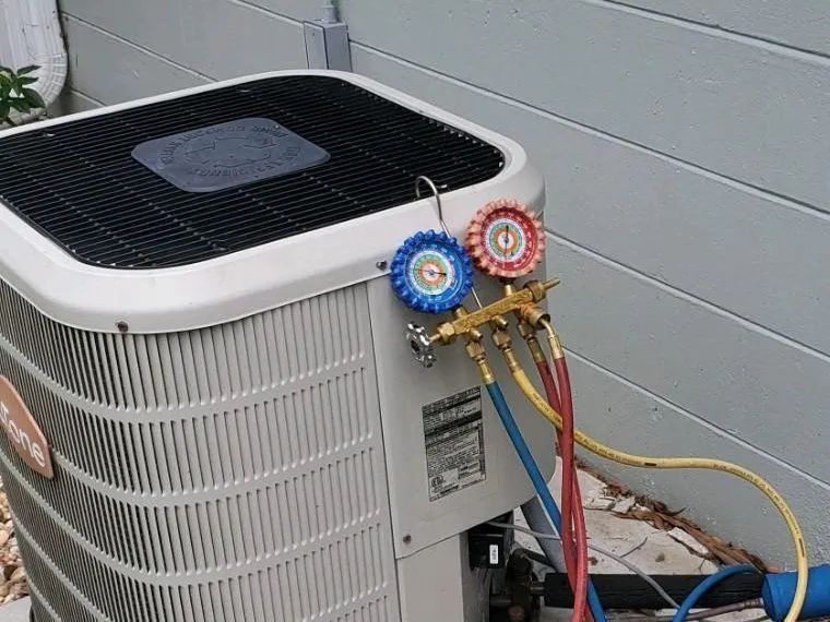Outdoor air conditioner unit with attached refrigerant gauges and colored hoses connected to the side