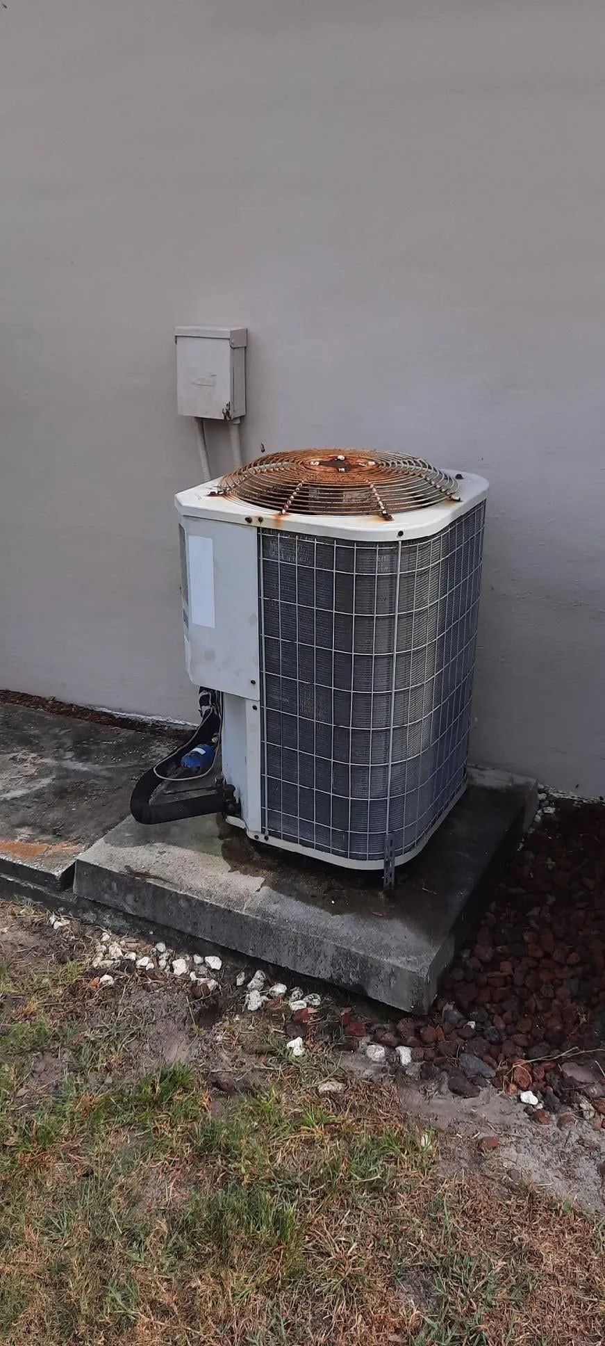 Outdoor air conditioner unit with debris piled on top beside a building wall