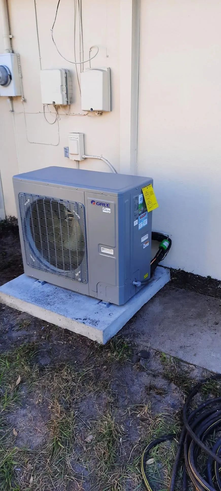 Outdoor HVAC unit on a concrete pad beside a wall with electrical boxes and wiring