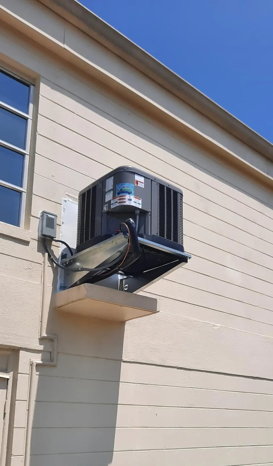 Wall-mounted HVAC unit on a beige building exterior under a blue sky.