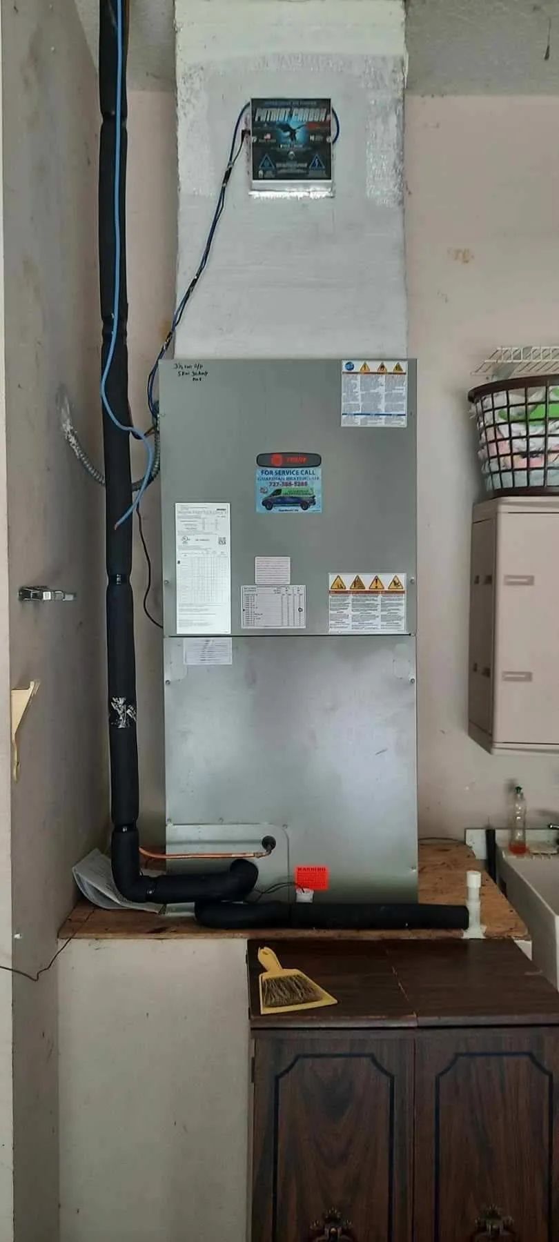 Gray wall-mounted water heater with pipes above a cabinet in a utility room