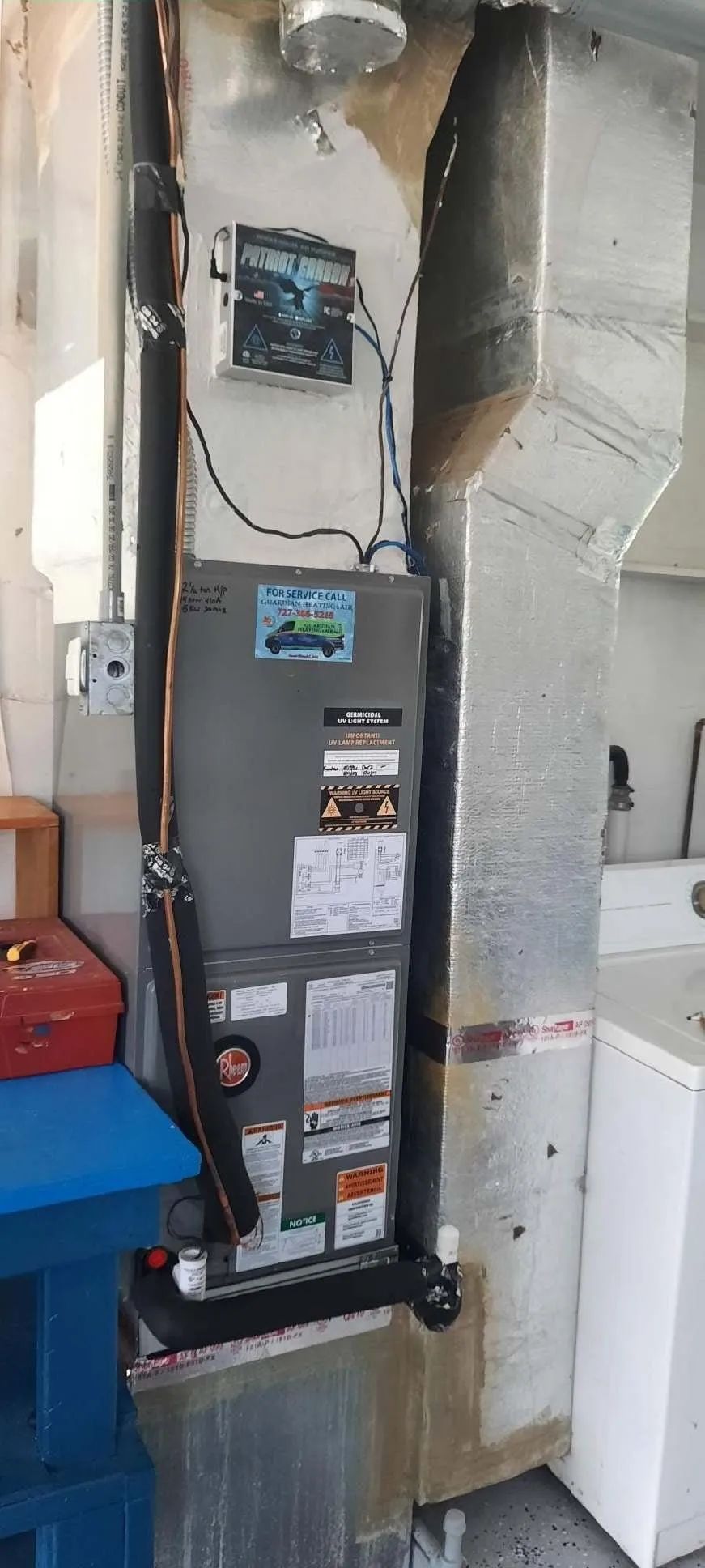 Wall-mounted furnace in a utility closet with exposed ductwork, pipes, and wires.