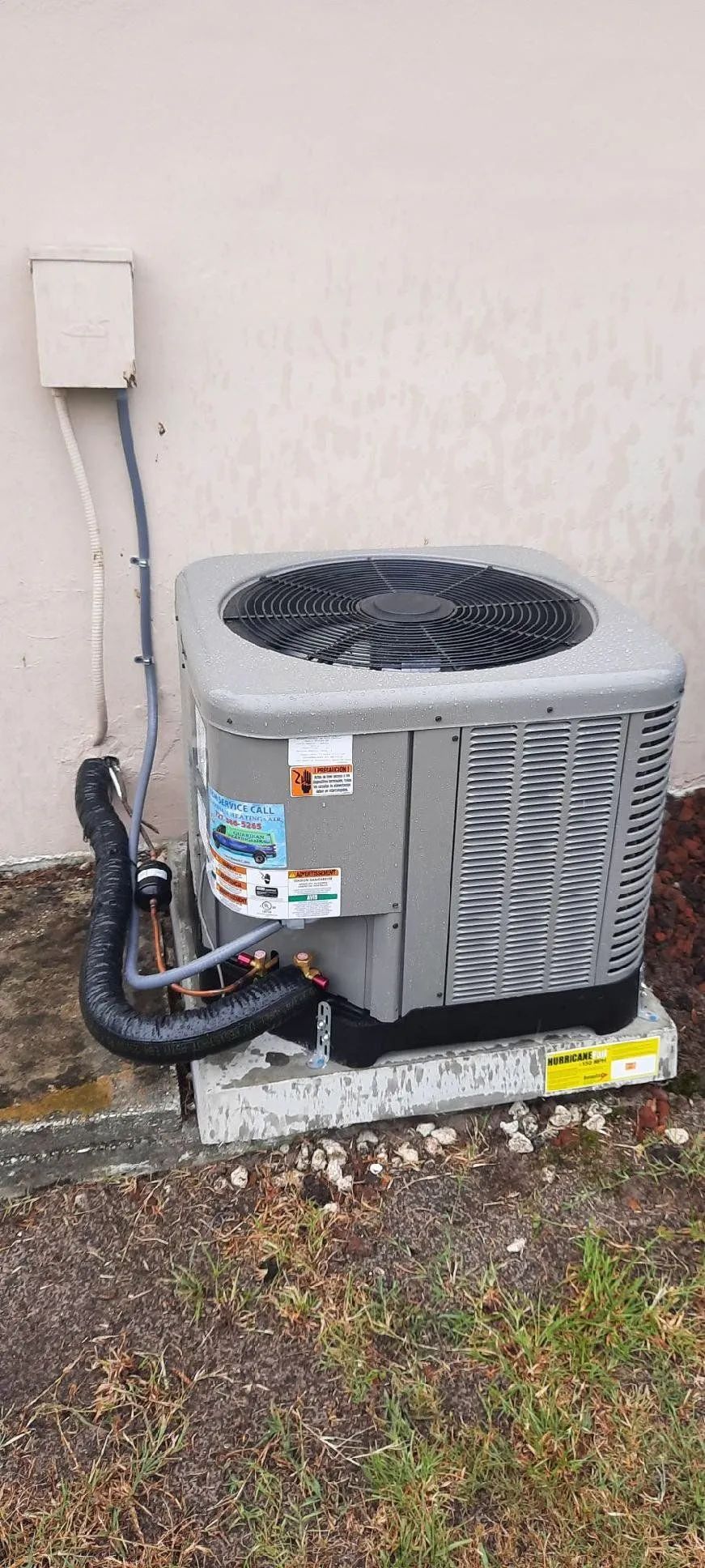 Outdoor HVAC condenser unit beside a house wall with electrical conduit and patchy grass nearby