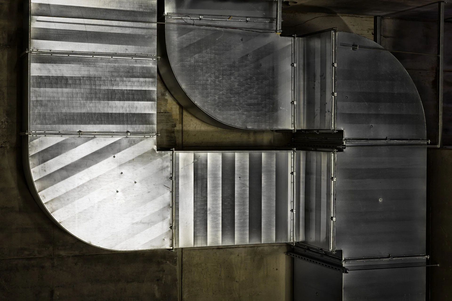 Abstract aerial view of curved metallic structures and striped surfaces in gray tones