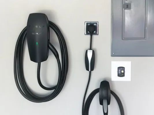 Wall-mounted electric vehicle charger with coiled black cable and plug on a light gray wall