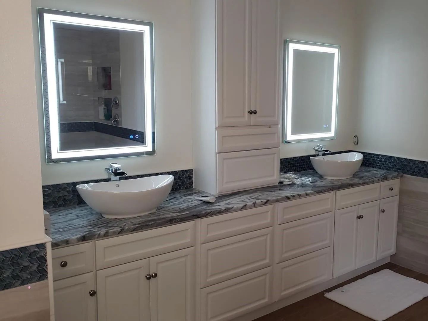 Bright bathroom vanity with two vessel sinks, illuminated mirrors, and white cabinetry