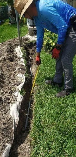 Worker in blue shirt and red gloves digging a trench beside a grassy lawn.