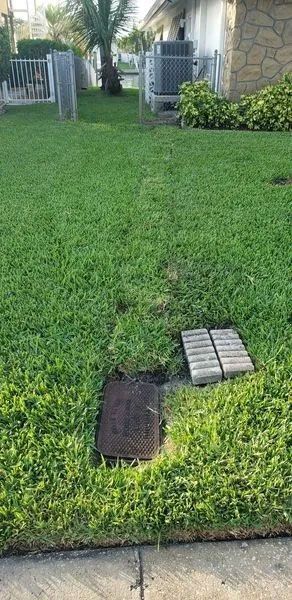 Grassy yard with utility covers near a house and fence