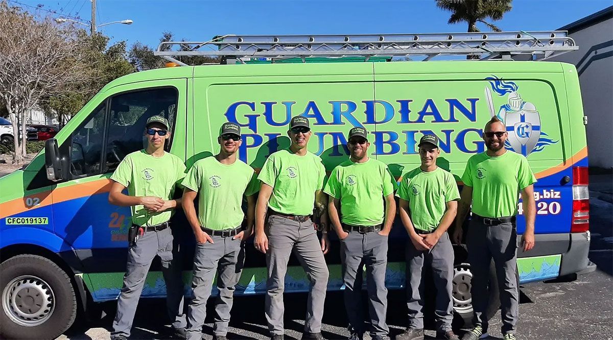 Five workers in green shirts stand beside a Guardian Plumbing service van.