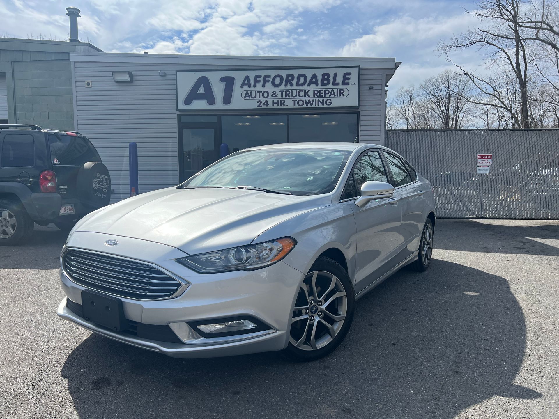 A silver ford fusion is parked in front of an auto repair shop.