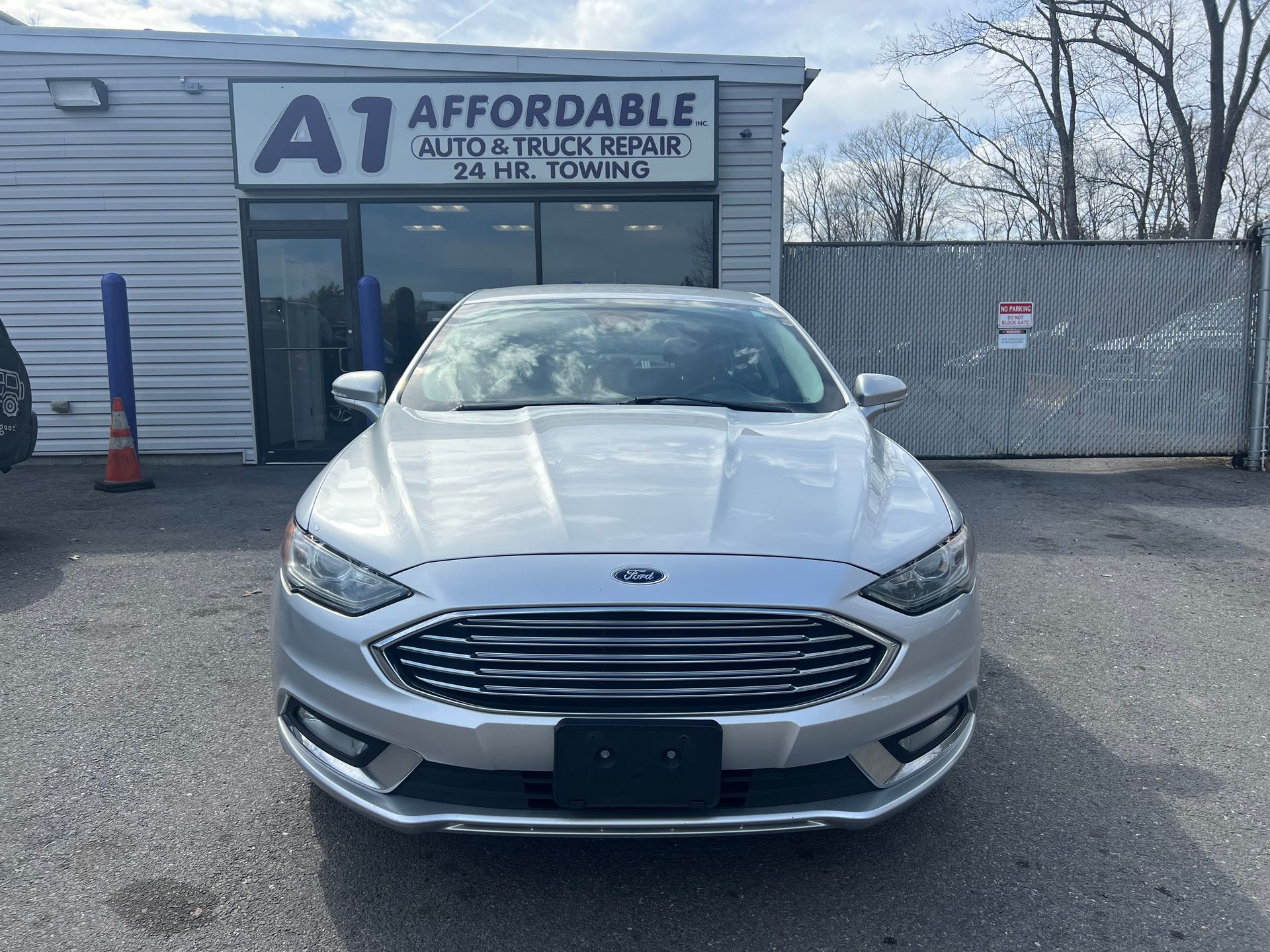 A silver ford fusion is parked in front of an auto shop.