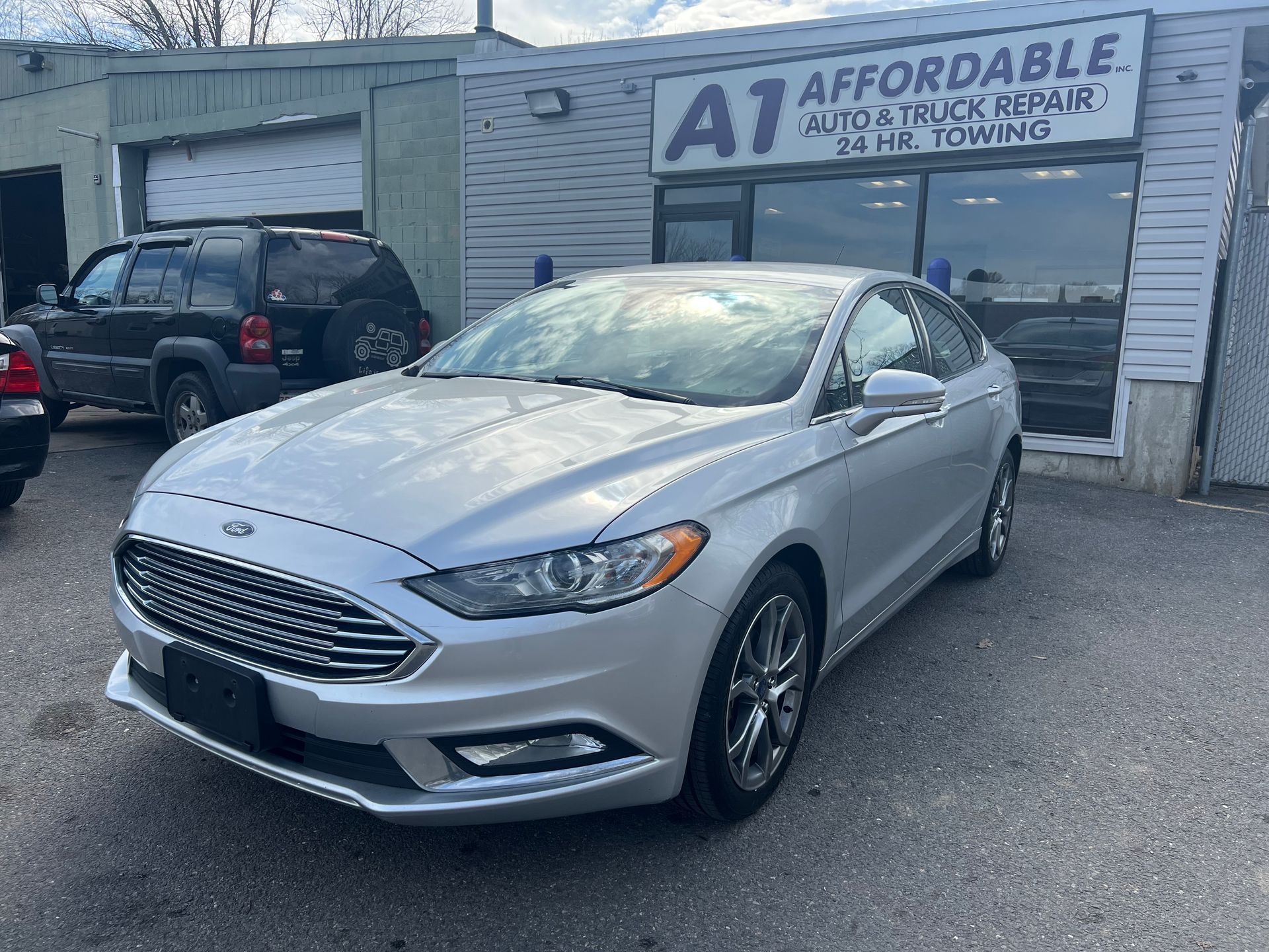 A silver ford fusion is parked in front of an auto shop.