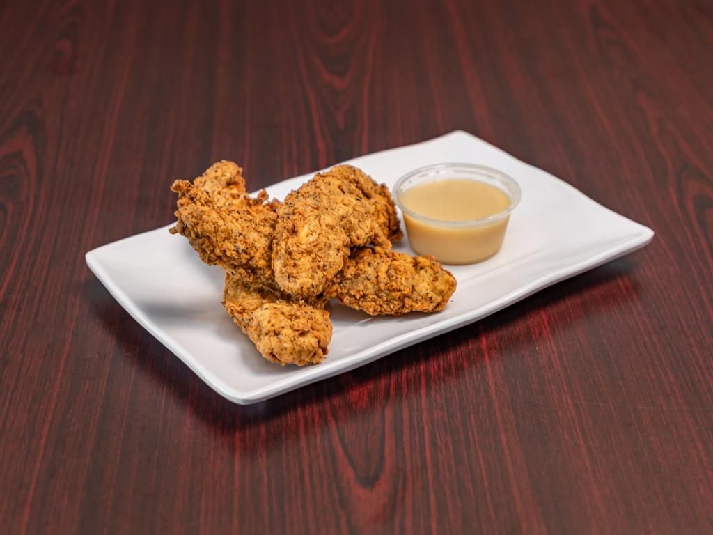 A white plate topped with chicken fingers and a dipping sauce on a wooden table.