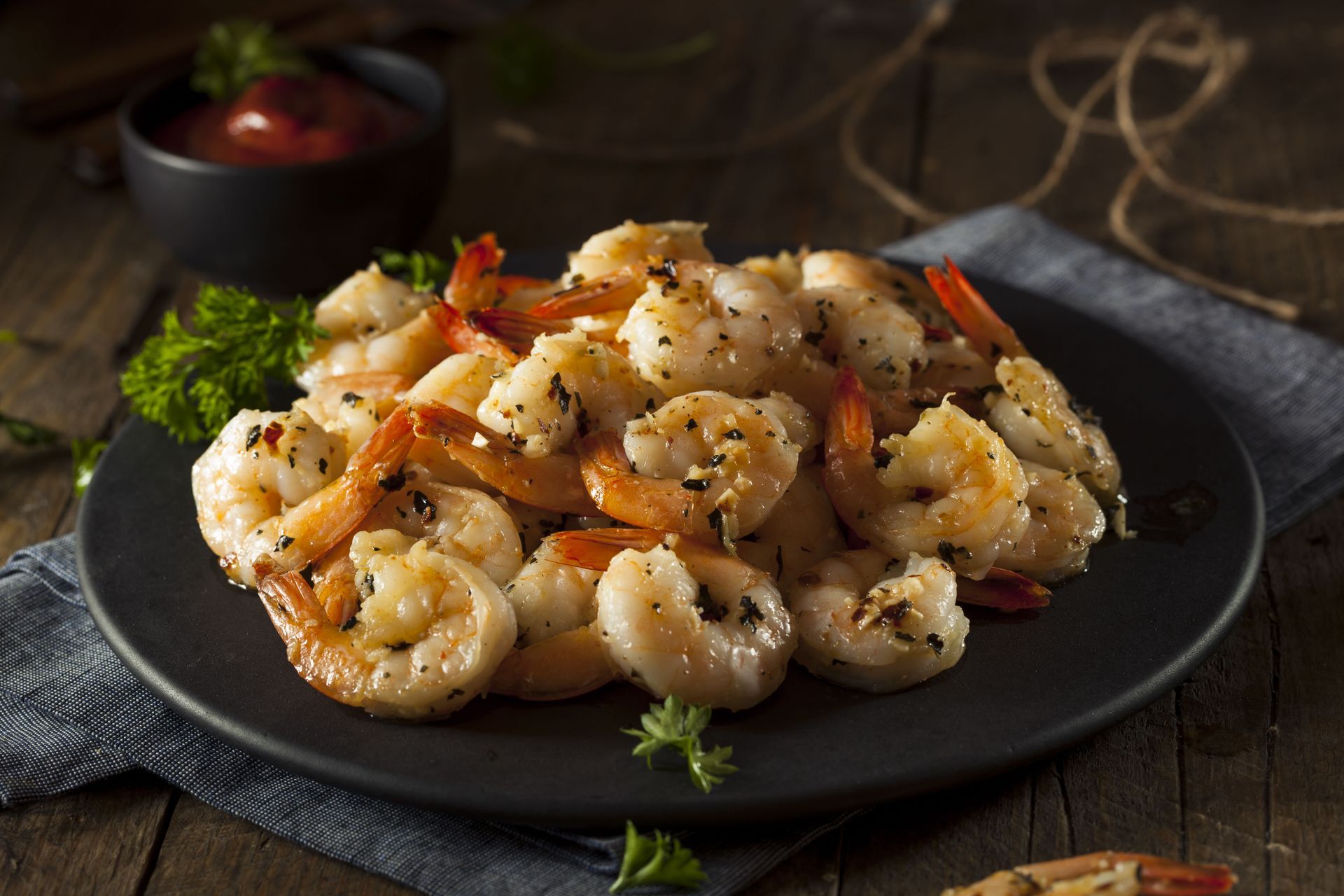 A black plate topped with cooked shrimp on a wooden table.