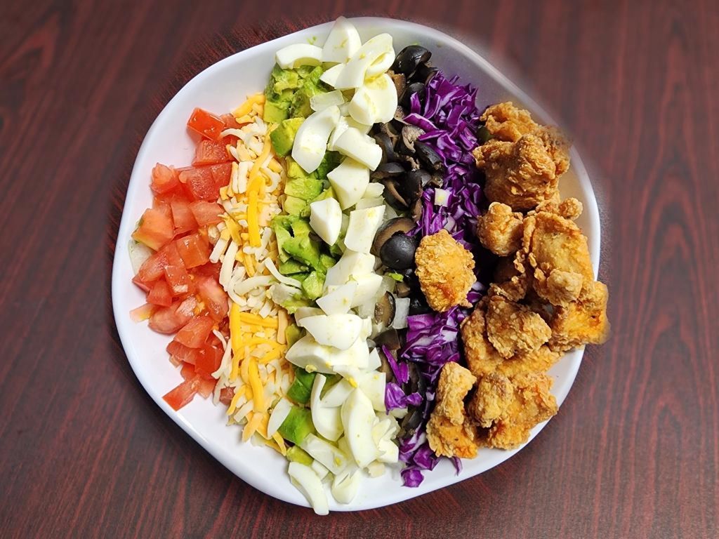 A white plate topped with a salad and fried chicken on a wooden table.