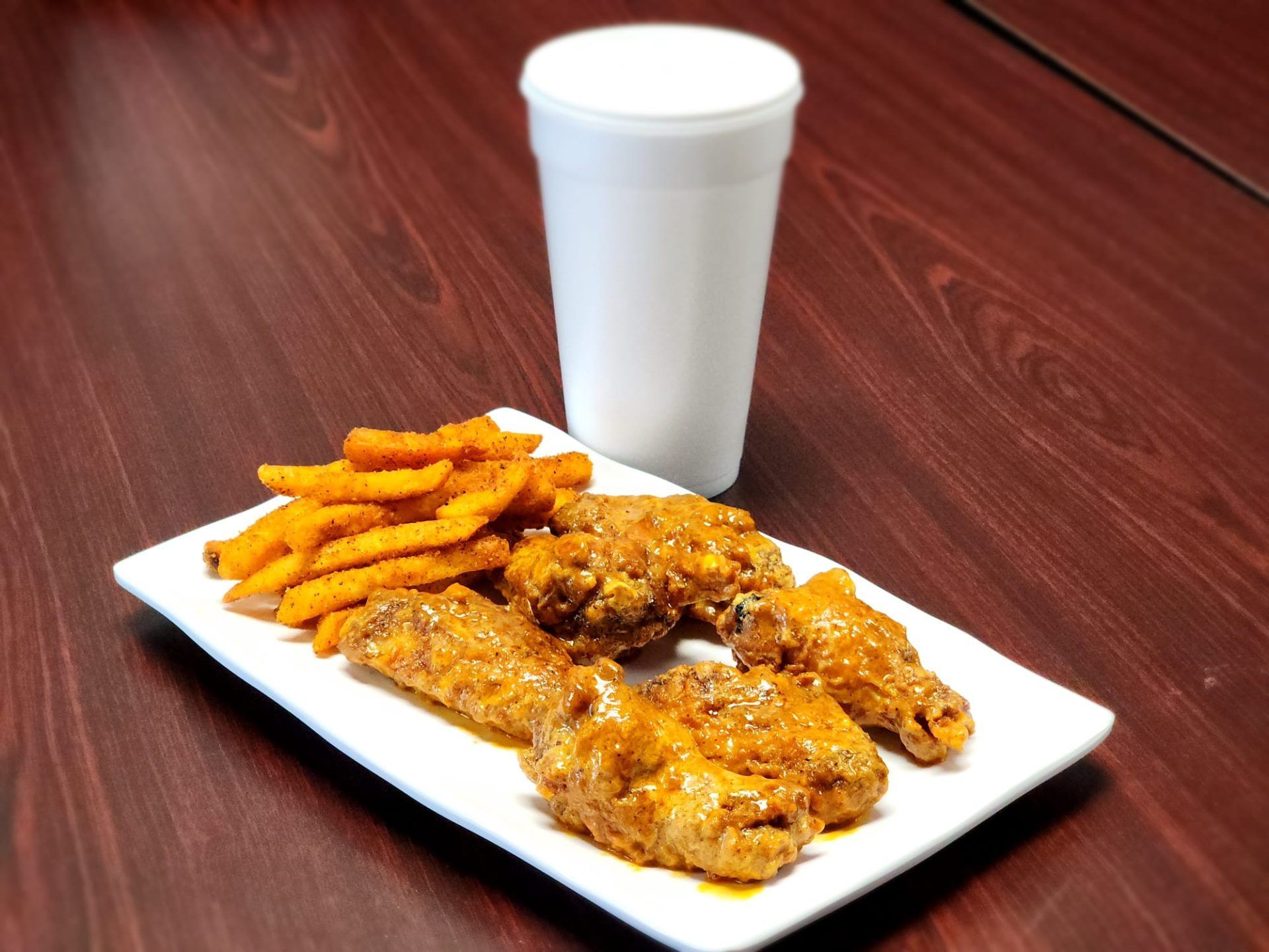 A plate of chicken wings and french fries next to a cup of soda