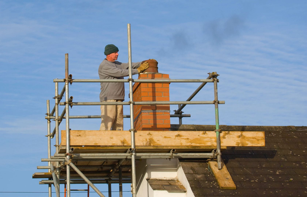 Worker on scaffolding repairing a chimney on a house roof under a blue sky