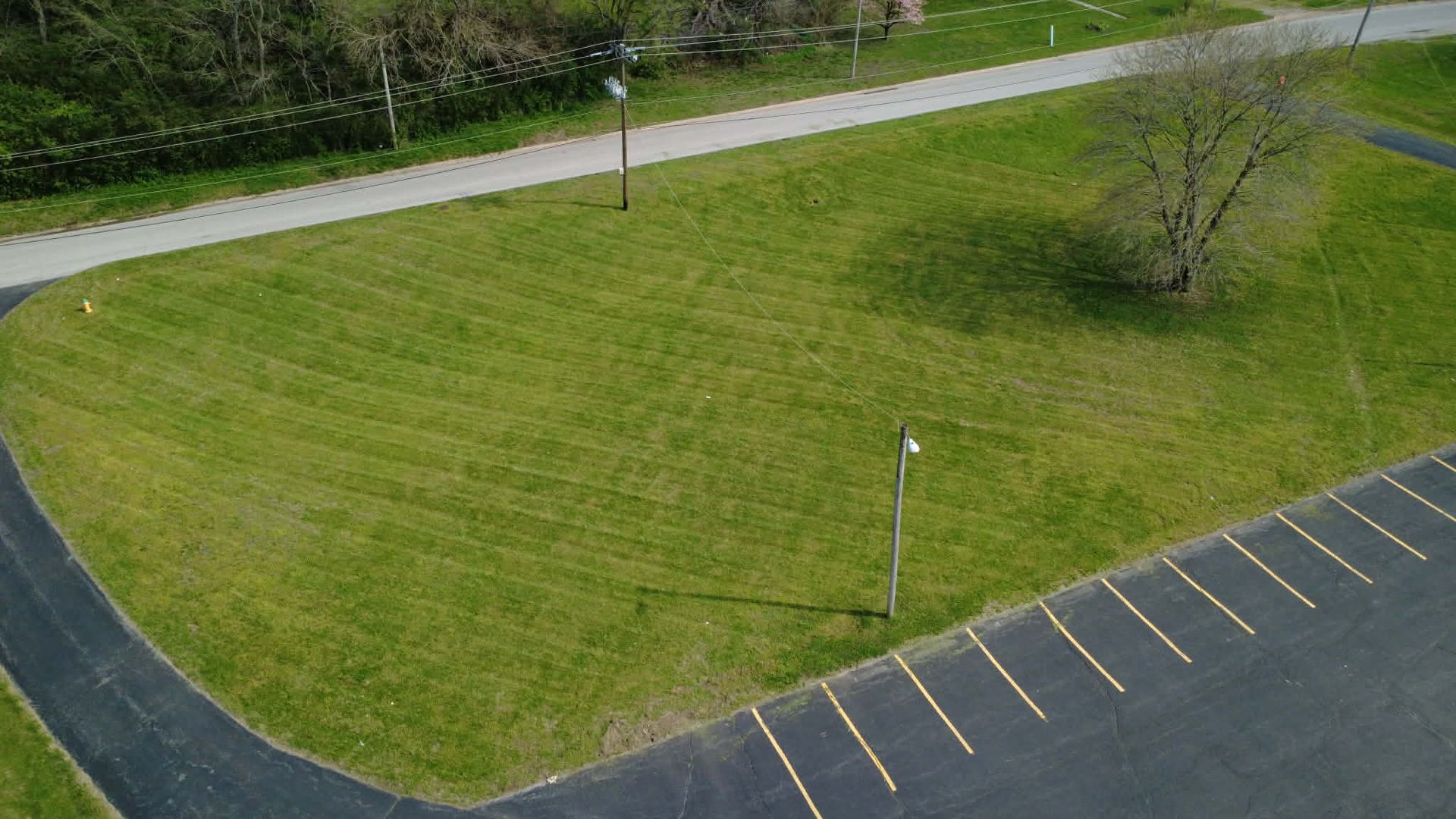 An aerial view of a green grassy lawn bordered by an asphalt path and a parking lot with painted yellow parking spaces.