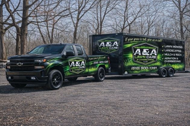 A black pickup truck towing an A&A Lawn Care branded trailer parked in a wooded area with trees in the background.