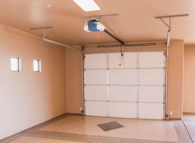 Empty beige garage with a closed white sectional door and tiled floor.